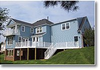 A large blue house with white trim and a raised deck.