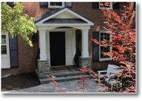 Front porch of a brick house with stone steps and white columns.