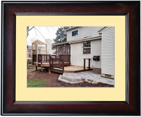 Backyard with wooden deck and stone patio next to a white house.
